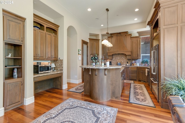 kitchen featuring a center island, hanging light fixtures, decorative backsplash, custom exhaust hood, and appliances with stainless steel finishes