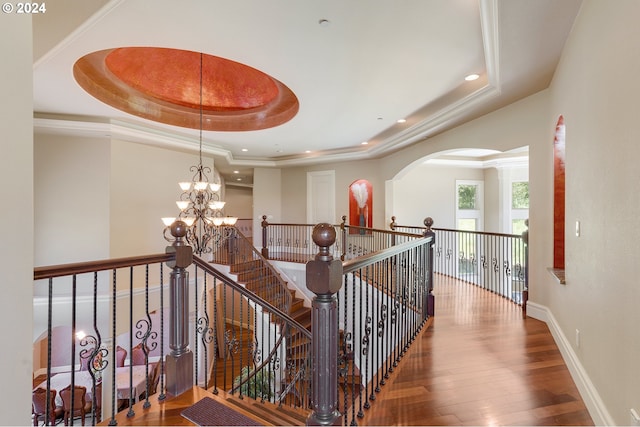 hall with a tray ceiling, wood-type flooring, and an inviting chandelier