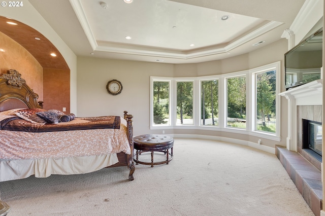 carpeted bedroom with a tray ceiling, a tile fireplace, and ornamental molding