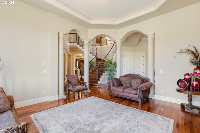 living room with a raised ceiling, crown molding, decorative columns, and hardwood / wood-style floors