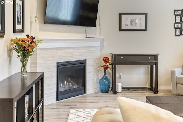 living area featuring a tile fireplace, baseboards, and wood finished floors