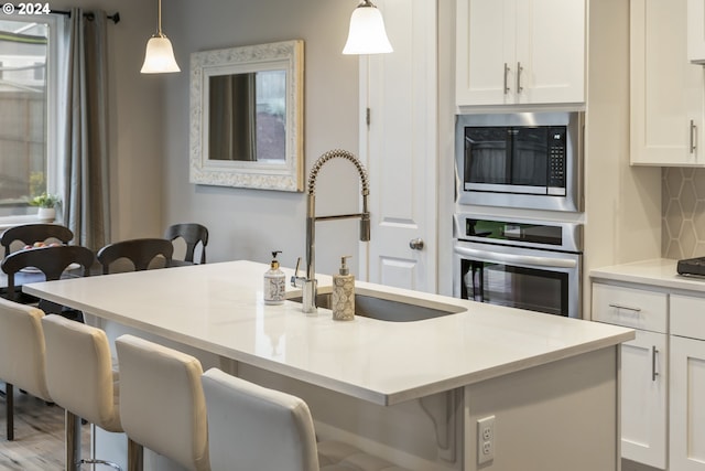 kitchen with built in microwave, a sink, decorative backsplash, oven, and white cabinets