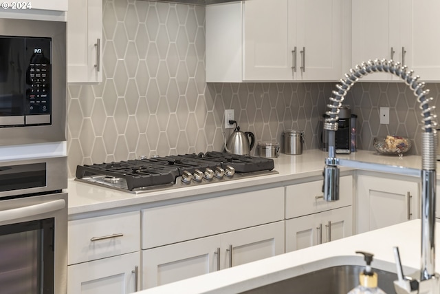 kitchen with backsplash, white cabinets, stainless steel appliances, and light countertops