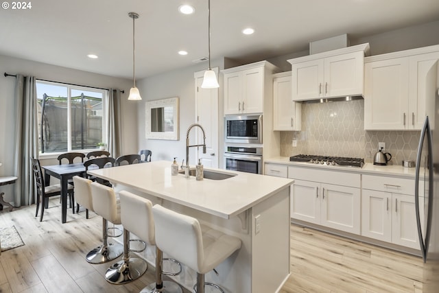 kitchen featuring a sink, stainless steel appliances, white cabinets, a kitchen bar, and light wood-type flooring