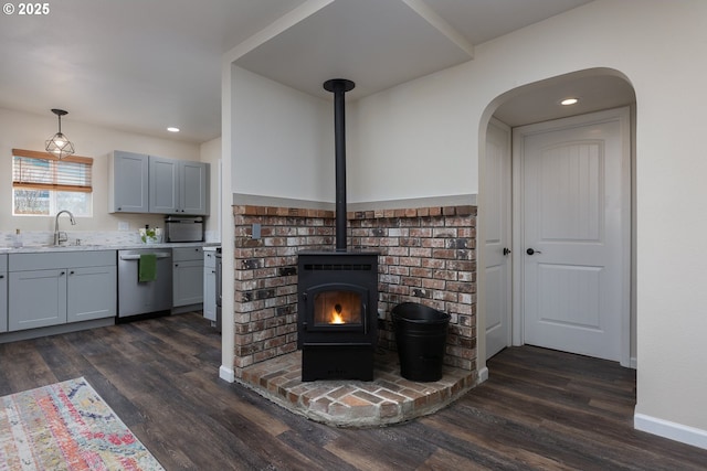 unfurnished living room with dark wood finished floors, a wood stove, baseboards, and a sink