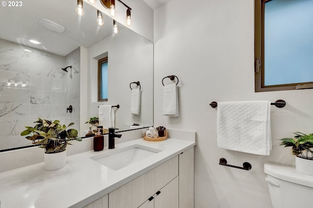 bathroom featuring a tile shower, vanity, and toilet