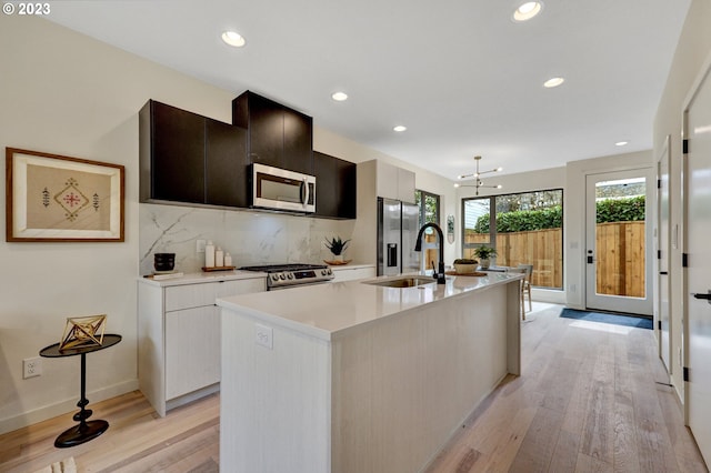 kitchen featuring stainless steel appliances, tasteful backsplash, a center island with sink, and light hardwood / wood-style floors