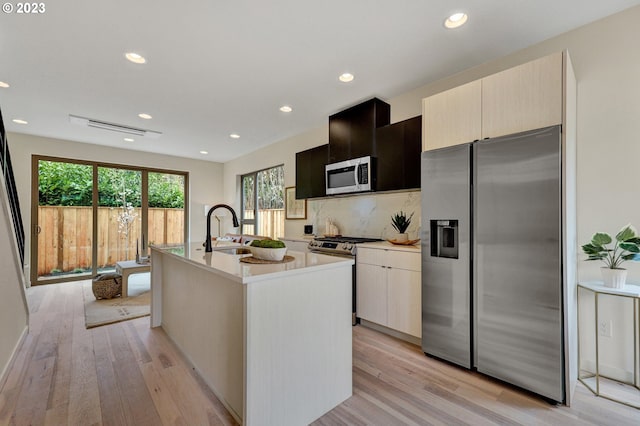 kitchen with a kitchen island with sink, a sink, stainless steel appliances, light countertops, and light wood-type flooring