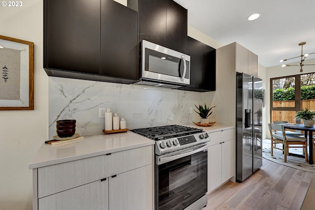 kitchen with light wood-style flooring, stainless steel appliances, light countertops, decorative backsplash, and dark cabinets