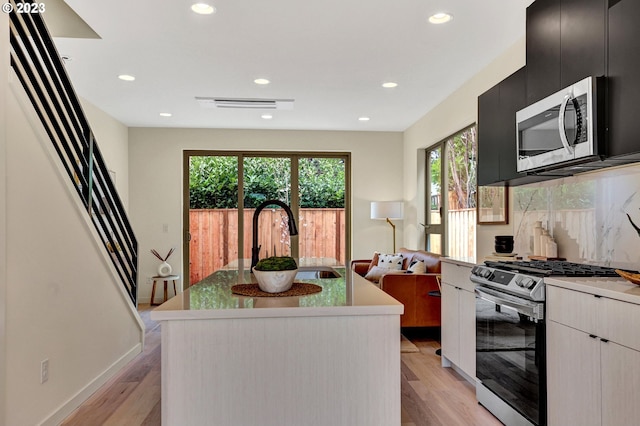 kitchen with a healthy amount of sunlight, appliances with stainless steel finishes, sink, a kitchen island, and light hardwood / wood-style floors