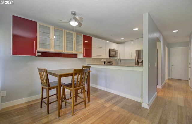 kitchen with ceiling fan, kitchen peninsula, tasteful backsplash, white cabinetry, and light hardwood / wood-style floors