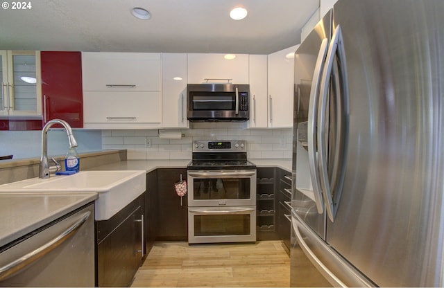 kitchen featuring sink, white cabinetry, light hardwood / wood-style flooring, decorative backsplash, and appliances with stainless steel finishes