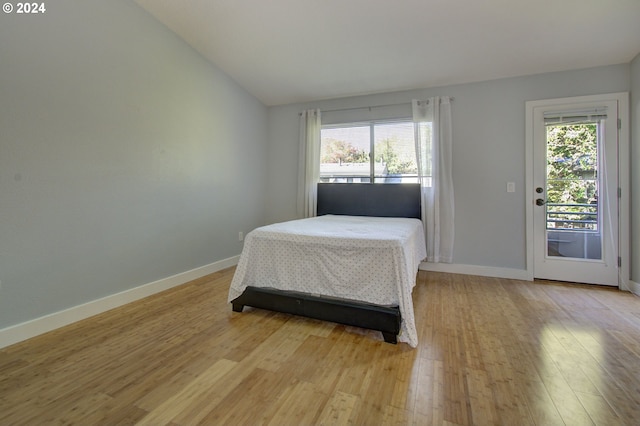 bedroom with multiple windows, light hardwood / wood-style floors, vaulted ceiling, and access to exterior