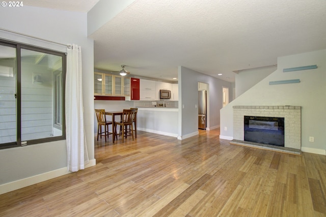 unfurnished living room with ceiling fan, a textured ceiling, a fireplace, and light hardwood / wood-style floors