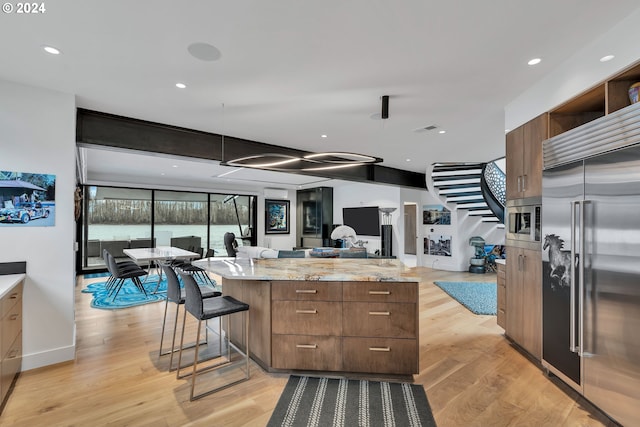 kitchen with a center island, light stone counters, stainless steel built in refrigerator, light hardwood / wood-style floors, and a breakfast bar