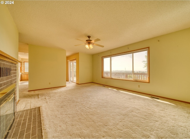 carpeted empty room with a textured ceiling, ceiling fan, and a fireplace