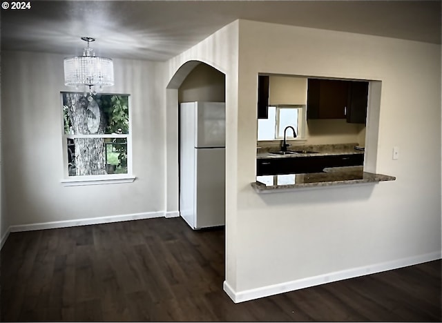 kitchen with dark wood-type flooring, light stone counters, stainless steel refrigerator, dark brown cabinets, and sink