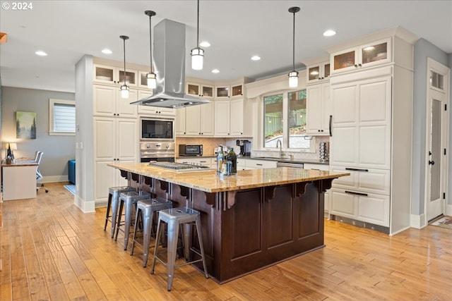 kitchen featuring appliances with stainless steel finishes, white cabinetry, a kitchen island, light stone counters, and island exhaust hood