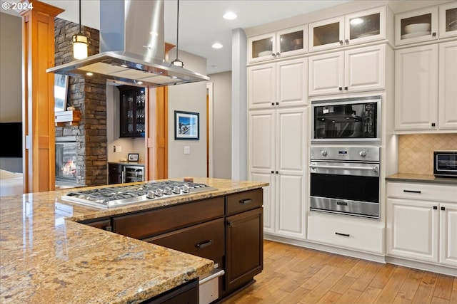 kitchen featuring appliances with stainless steel finishes, white cabinetry, hanging light fixtures, island exhaust hood, and light hardwood / wood-style floors