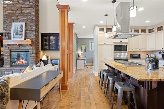 kitchen featuring light stone counters, island range hood, pendant lighting, stainless steel appliances, and white cabinets