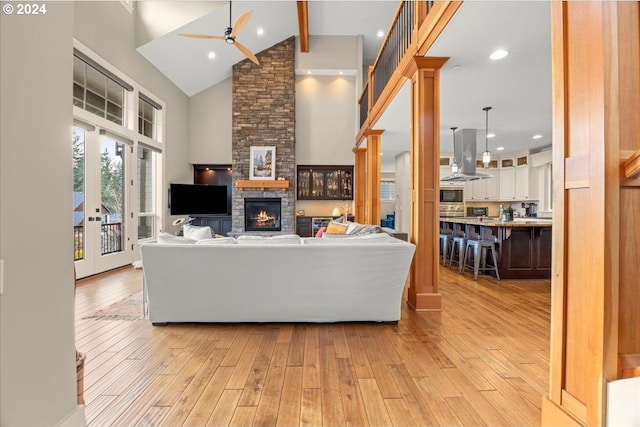 living room featuring high vaulted ceiling, light hardwood / wood-style flooring, beamed ceiling, ceiling fan, and a fireplace