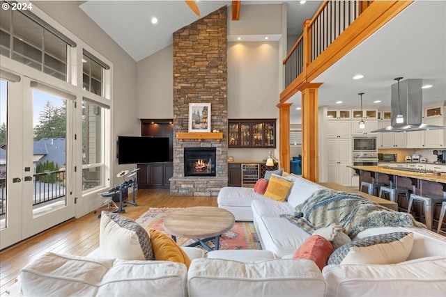 living room featuring high vaulted ceiling, beverage cooler, a fireplace, and light hardwood / wood-style flooring