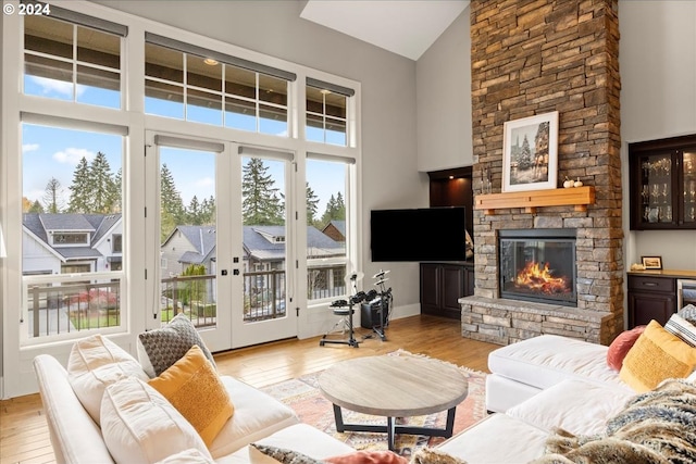 living room featuring a stone fireplace, high vaulted ceiling, french doors, and light wood-type flooring