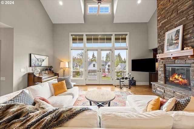 living room with french doors, a towering ceiling, a fireplace, and light hardwood / wood-style flooring