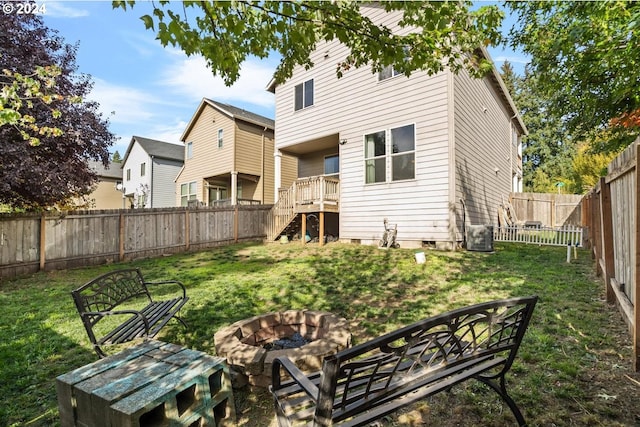 back of property featuring a fire pit, cooling unit, a deck, and a lawn