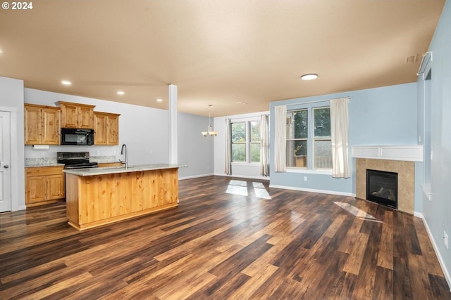 kitchen featuring stainless steel gas range, dark wood-type flooring, decorative light fixtures, a fireplace, and an island with sink