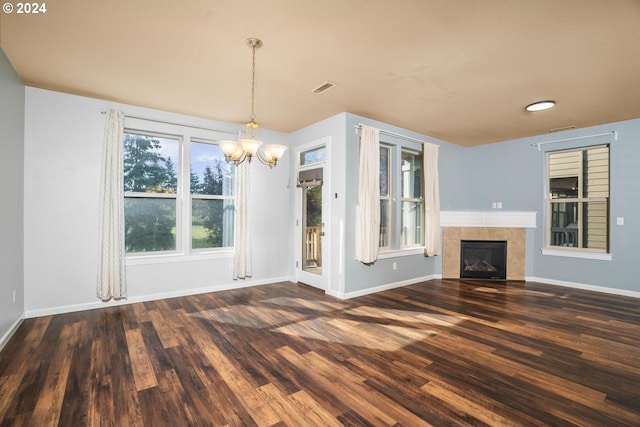 unfurnished living room with dark hardwood / wood-style flooring, an inviting chandelier, and a tiled fireplace