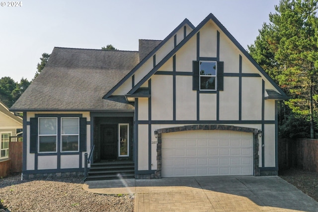 tudor-style house with concrete driveway, roof with shingles, and stucco siding