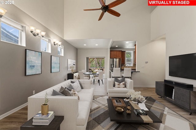 living room with baseboards, a high ceiling, recessed lighting, and light wood-style floors