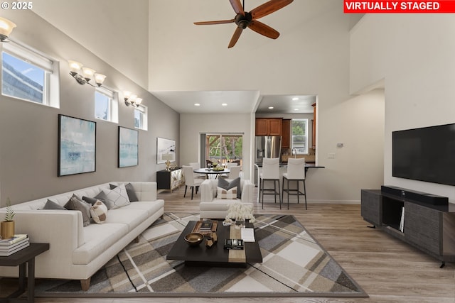 living room with a towering ceiling, light wood finished floors, baseboards, and recessed lighting