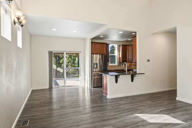 kitchen with a breakfast bar area, dark wood-type flooring, open floor plan, stainless steel refrigerator with ice dispenser, and dark countertops