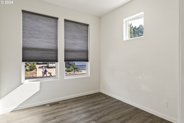 unfurnished room with a wealth of natural light, visible vents, baseboards, and wood finished floors