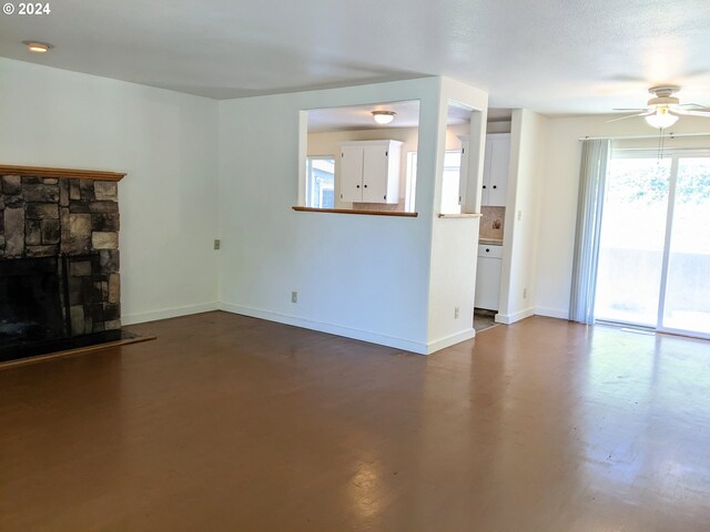 unfurnished living room with ceiling fan and a stone fireplace