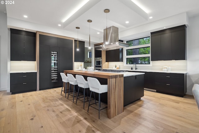 kitchen with tasteful backsplash, light hardwood / wood-style floors, island range hood, decorative light fixtures, and butcher block countertops