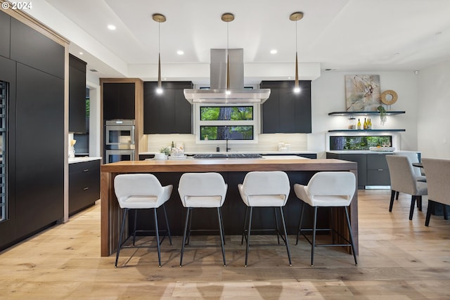 kitchen with island range hood, a center island, decorative light fixtures, and light hardwood / wood-style flooring