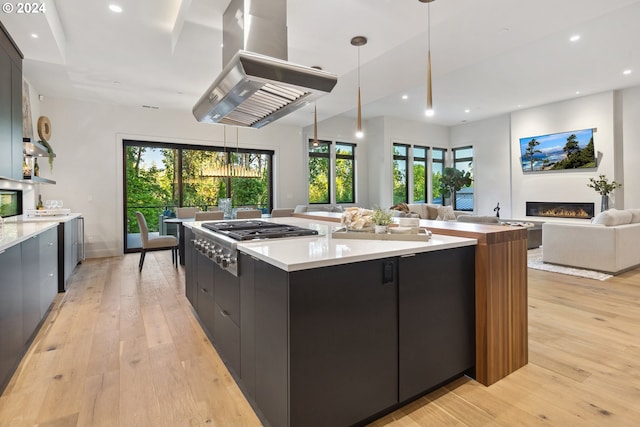 kitchen with stainless steel gas stovetop, decorative light fixtures, island exhaust hood, and light hardwood / wood-style flooring