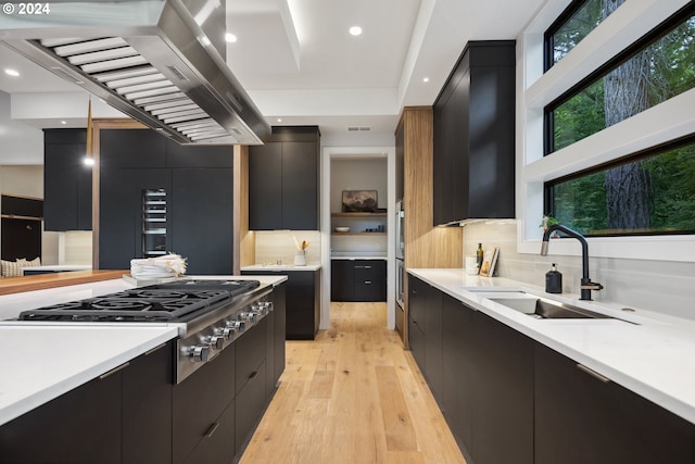 kitchen featuring backsplash, wall chimney exhaust hood, stainless steel gas cooktop, sink, and light hardwood / wood-style flooring