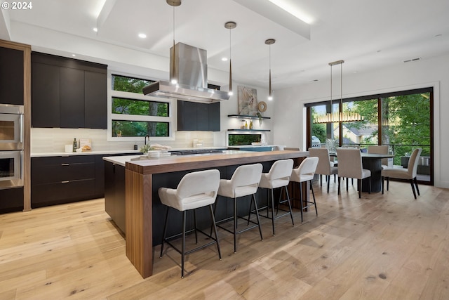 13581 Goodall Rd, Lake Oswego, OR 97034 - kitchen featuring wood counters, island exhaust hood, a spacious island, backsplash, and light wood-type flooring