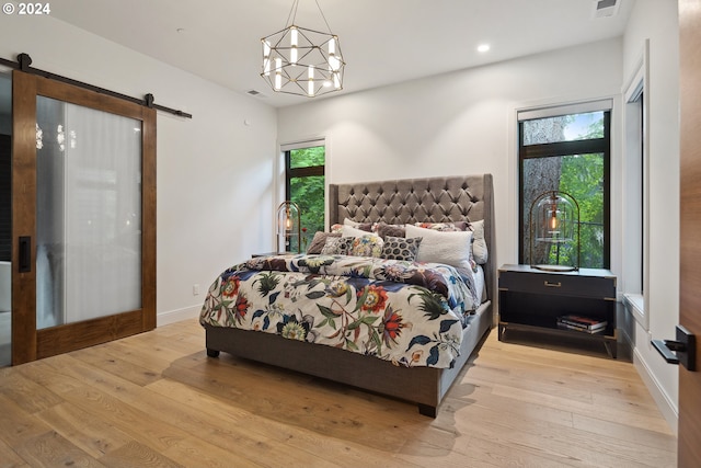 bedroom with a barn door, a chandelier, light hardwood / wood-style floors, and multiple windows