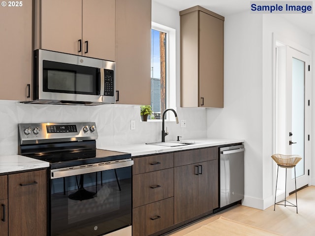 kitchen with appliances with stainless steel finishes, a sink, decorative backsplash, light wood finished floors, and light stone countertops