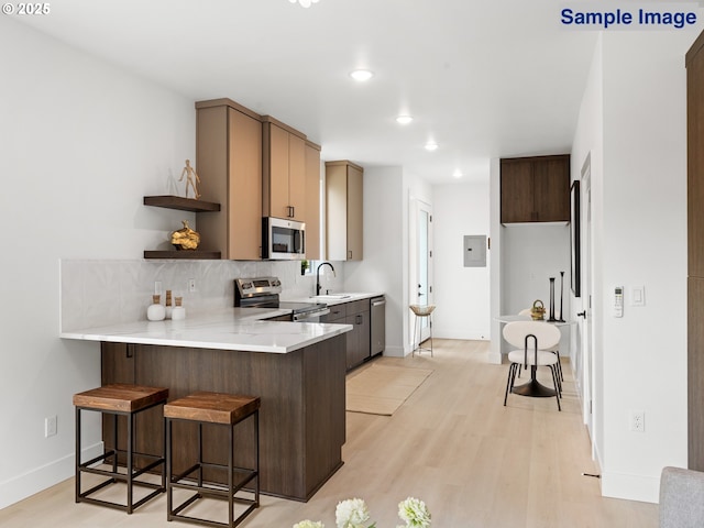 kitchen with stainless steel appliances, a sink, open shelves, a breakfast bar area, and a peninsula