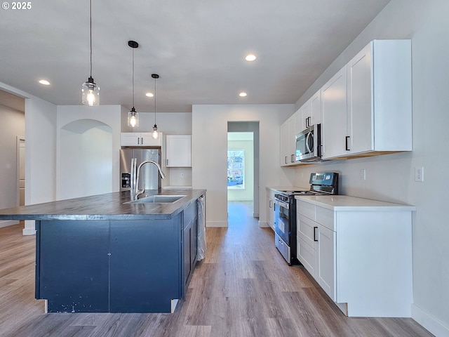 kitchen featuring a sink, stainless steel appliances, arched walkways, and light wood-style floors