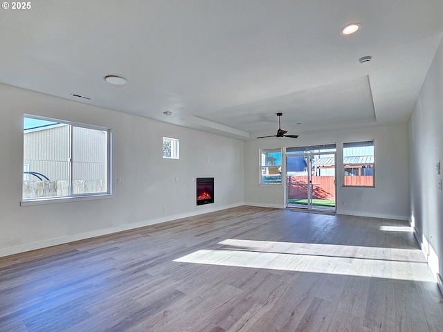 unfurnished living room featuring wood finished floors, baseboards, and a lit fireplace