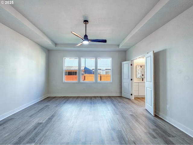 unfurnished bedroom with a tray ceiling, baseboards, wood finished floors, and a ceiling fan