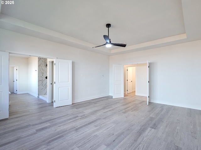 unfurnished room featuring a ceiling fan, a raised ceiling, wood finished floors, and baseboards