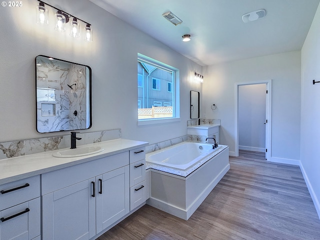 bathroom featuring two vanities, a sink, wood finished floors, a marble finish shower, and a bath